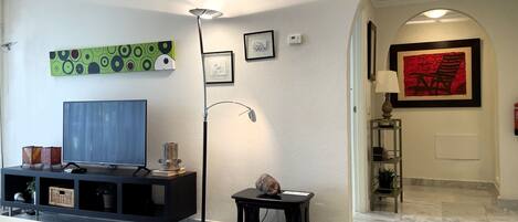 Ein Wohnzimmer mit Flachbildfernseher, einer Stehlampe, einer dekorativen Schale und einem gerahmten Kunstwerk an der Wand.