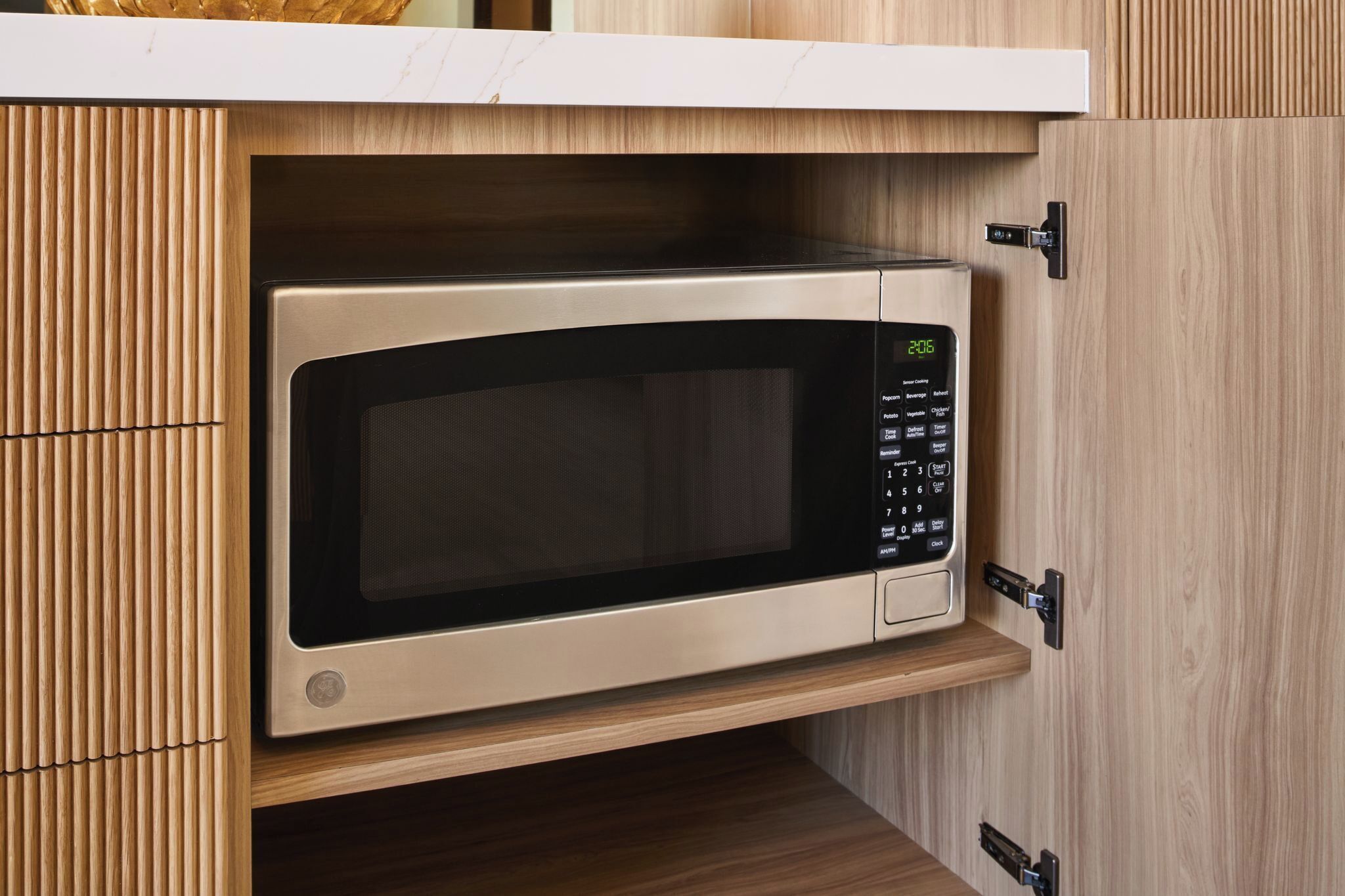 A microwave oven installed in a wooden cabinet with a digital display.