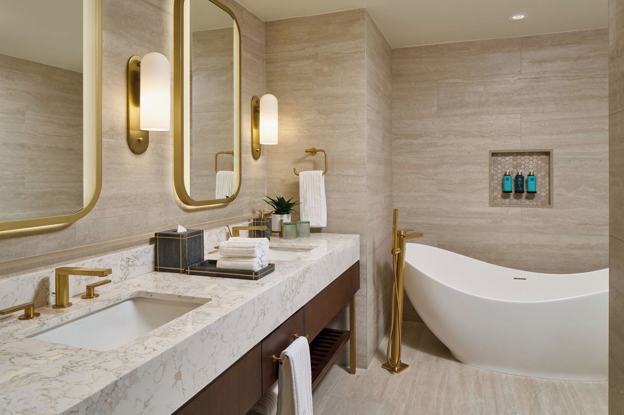 A modern bathroom with a freestanding bathtub, a large mirror with gold frame, and a marble countertop with two sinks.
