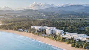 Vista aérea de un complejo turístico costero con varias edificaciones, una playa y vegetación circundante.