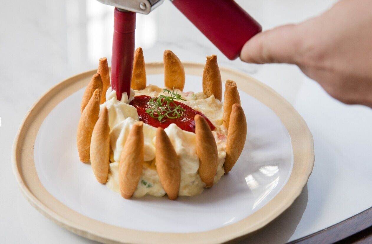 A dessert with a red piping tool, a plate, and a hand.
