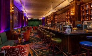 Uma área de bar com um balcão extenso, vários bancos e uma adega abastecida com garrafas.