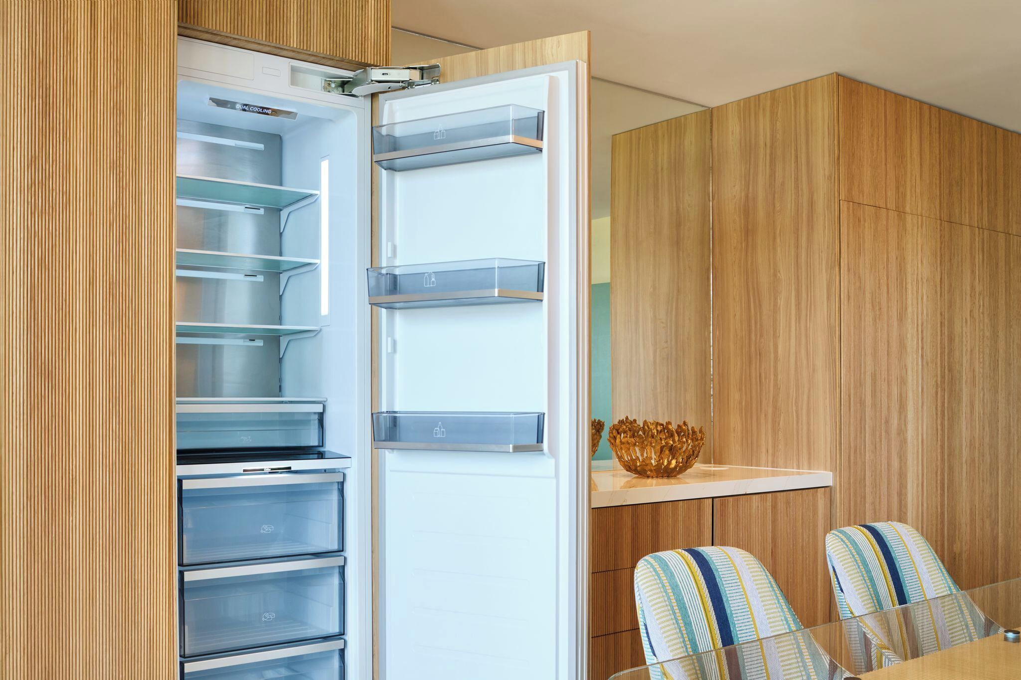 Una cocina moderna con refrigerador integrado, armarios de madera y un comedor con sillas a rayas.