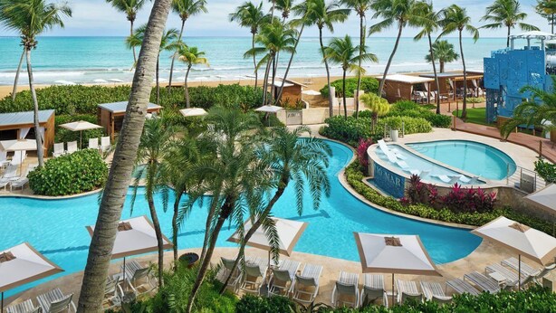 Un resort con piscina, palmeras y vista a la playa.