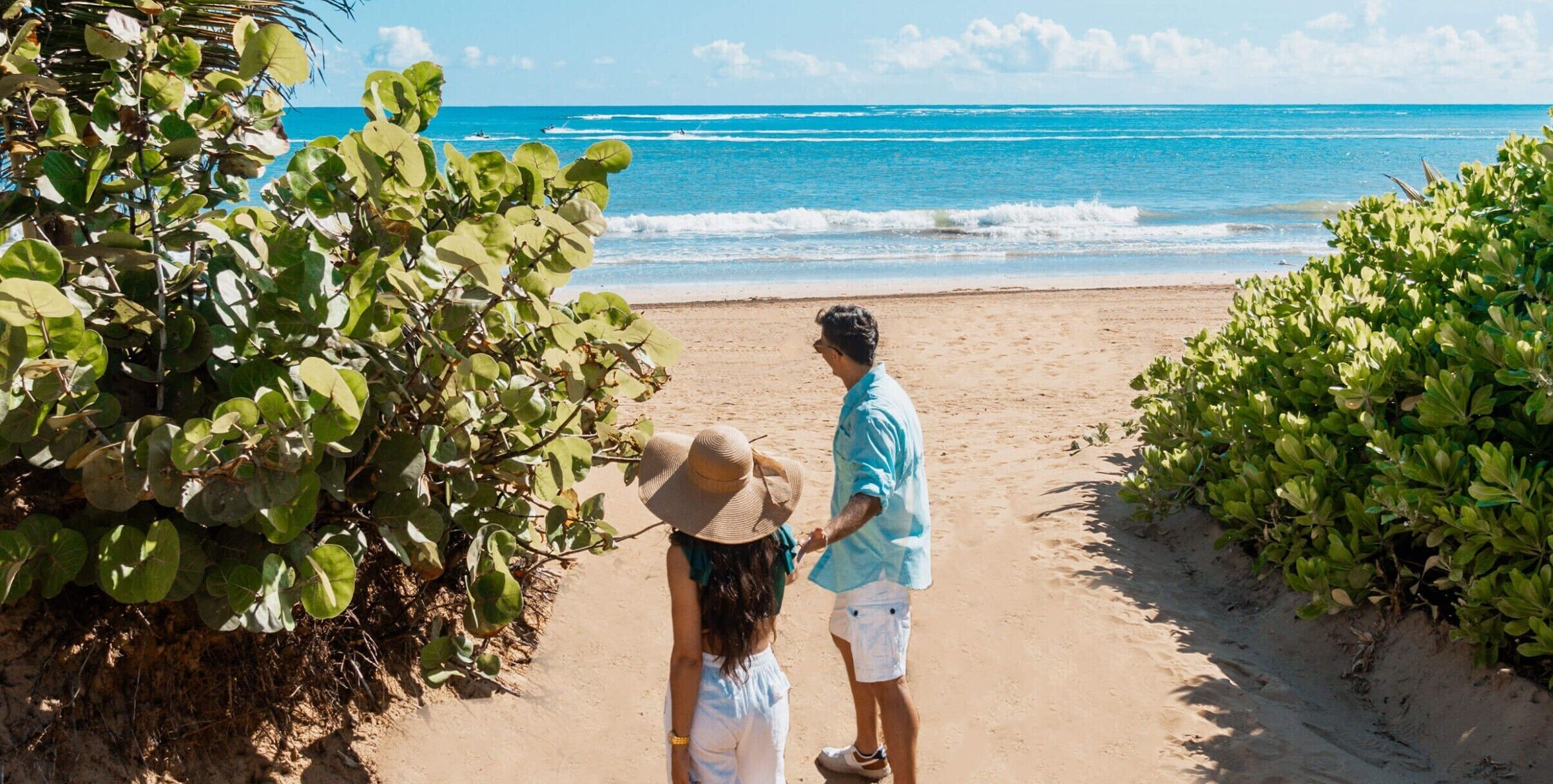 A couple walking on a sandy beach with ocean waves in the background.