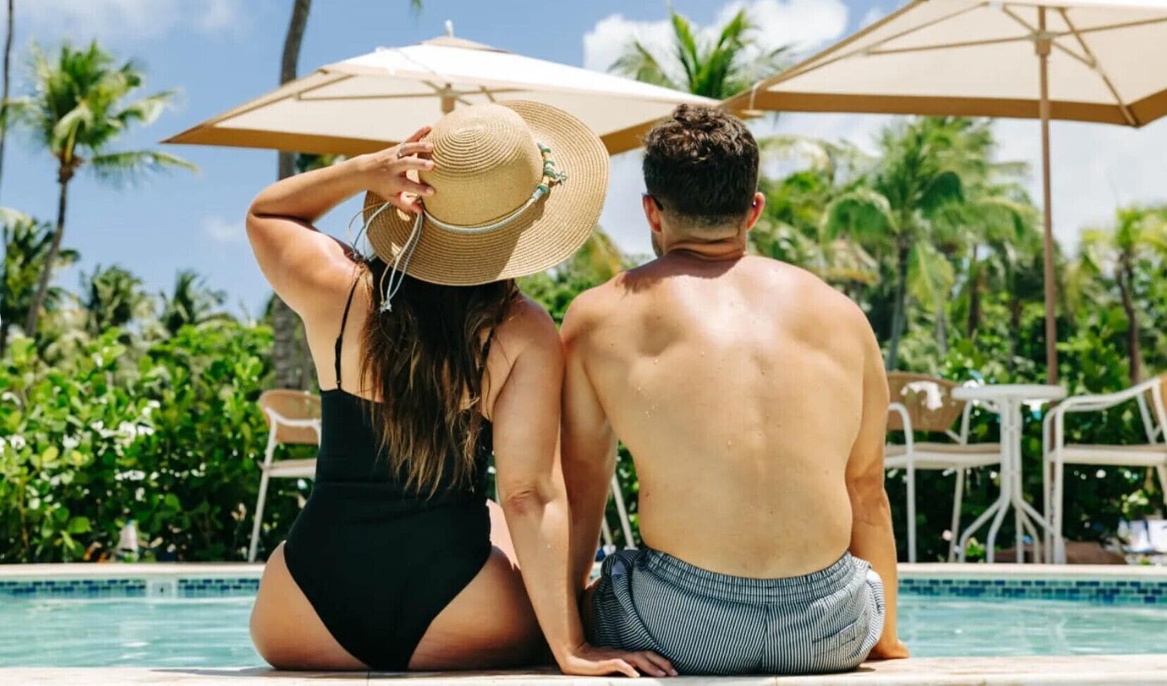 A couple sitting by a pool with umbrellas, surrounded by greenery.