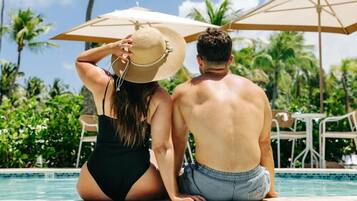 A couple sitting by a pool with umbrellas, surrounded by greenery.