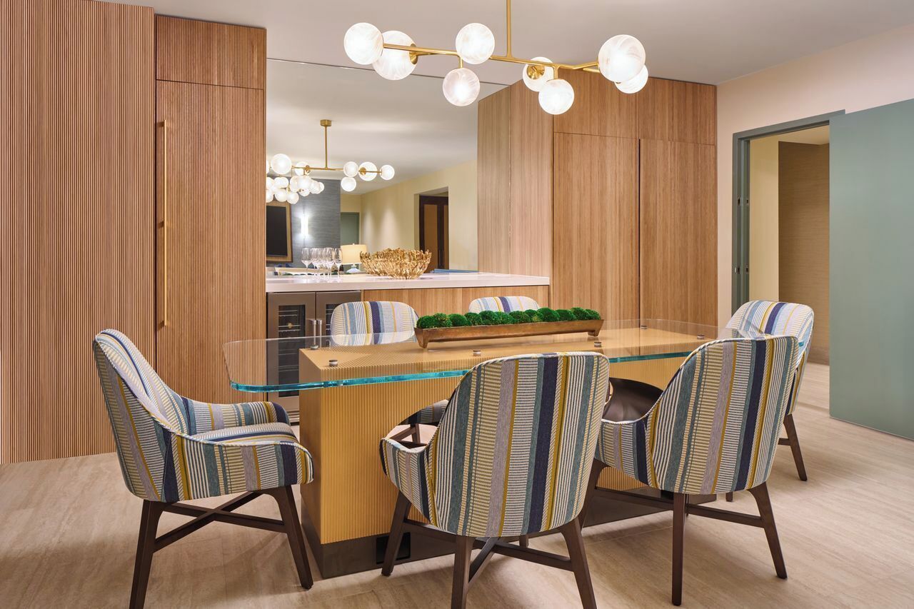 A modern dining area with a glass table, striped chairs, and a central island with a bowl and plants.
