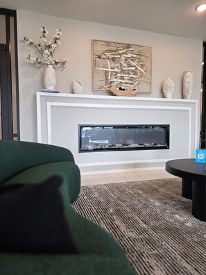 A modern living room with a fireplace, a green sofa, a round coffee table, and decorative items on the mantel. - Modern Escape Near Waterpark (Houston)