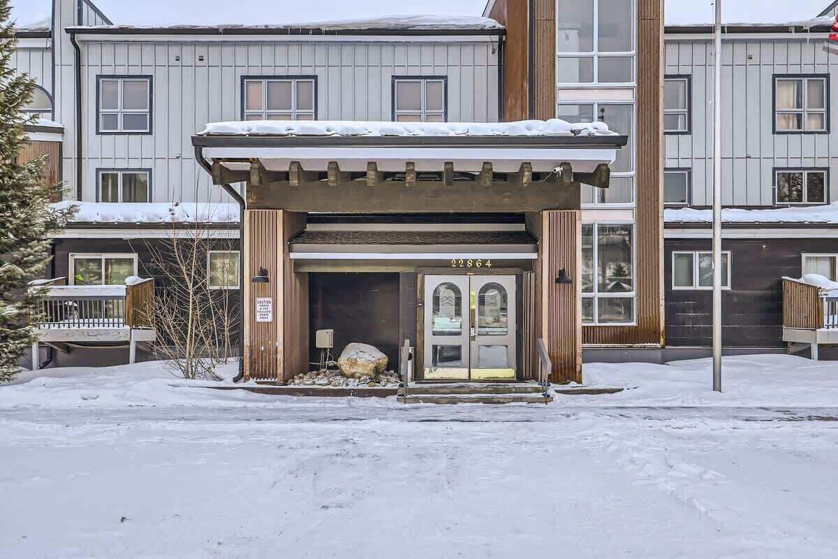 A building with a snow-covered entrance, a wooden structure with the number 22864, and a multi-story background.
