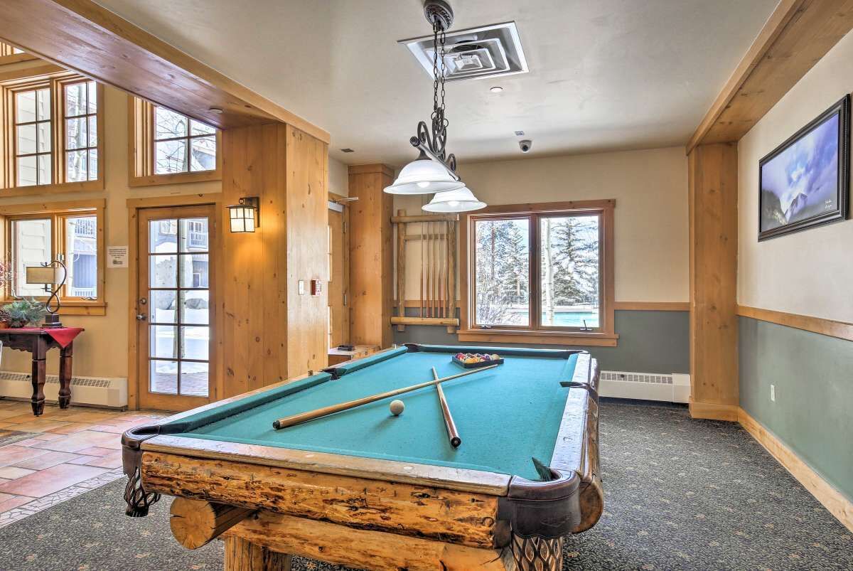 A pool table in a room with wooden walls and large windows.