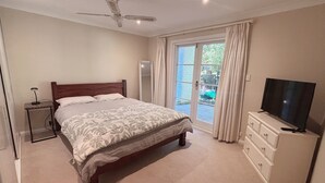A bedroom with a bed, a ceiling fan, a television on a dresser, and a sliding glass door to the outside.