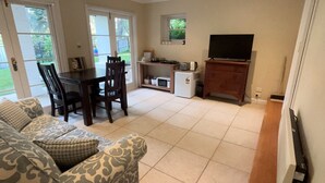 A living room with a sofa, a dining table, chairs, a TV, and a kitchen area with a microwave and toaster.
