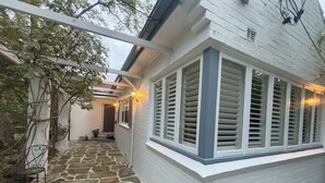 A house with a stone pathway leading to a covered porch, a window with shutters, and a door.