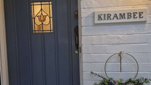 A dark blue door with a decorative glass panel, a white brick wall, and a sign reading 'KIRAMBEE'.