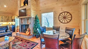 A wooden cabin interior with a fireplace, a Christmas tree, a dining table with chairs, and a large wooden wheel on the wall. - Luxury Mineral Bluff Cabin with Hot Tub and Decks (Mineral Bluff)