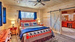 A wooden cabin bedroom with a bed, bedside lamps, a desk, and a mirror. - Luxury Mineral Bluff Cabin with Hot Tub and Decks (Mineral Bluff)