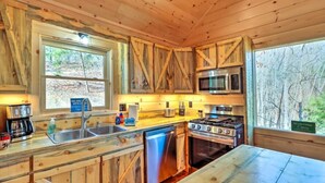 A wooden cabin kitchen with a sink, stove, microwave, and a view of the forest. - Luxury Mineral Bluff Cabin with Hot Tub and Decks (Mineral Bluff)