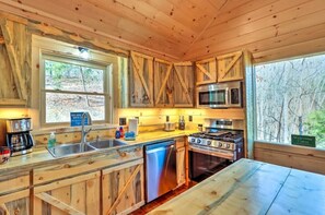 Eine Holzblockküche mit Spüle, Herd, Mikrowelle und Blick auf den Wald.