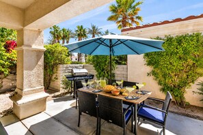 Eine Außenpatio mit Esstisch, Grill und einem blauen Sonnenschirm.