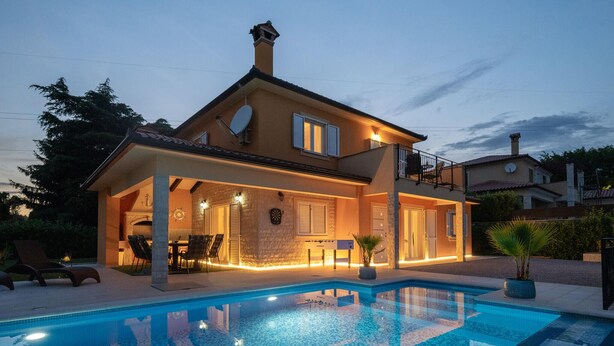 Ein zweistöckiges Haus mit Swimmingpool, Sitzgelegenheiten im Freien und einem Balkon.