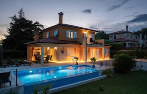 Una casa de dos pisos con piscina, mobiliario exterior y antenas parabólicas.