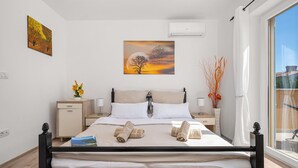 Ein ordentlich bezogenes Bett mit Handtüchern, ein Nachttisch mit Lampe, ein Gemälde über dem Bett und ein Fenster mit Aussicht.