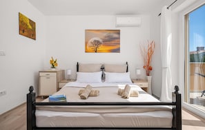 Una cama bien hecha con toallas, una mesita de noche con lámpara, un cuadro sobre la cama y una ventana con vistas.