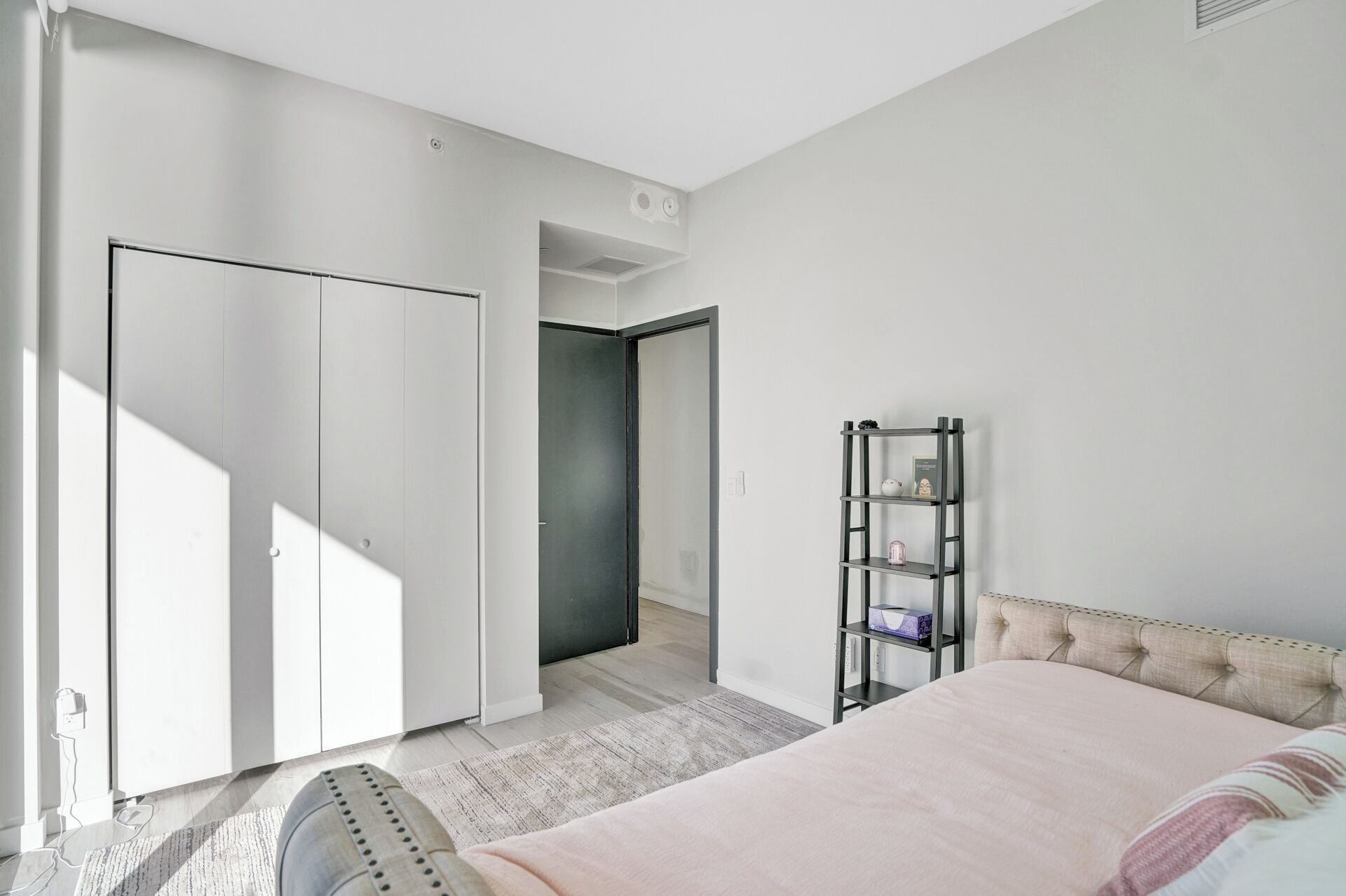 A bedroom with a bed, a wardrobe, a shelf, and a door leading to another room.