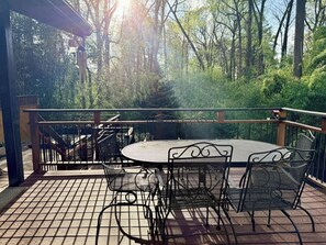 A covered outdoor patio with a round table and chairs, surrounded by a wooden deck and metal railing.