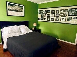 A neatly made bed with white linens, a black headboard, and a framed picture of a mountain on the wall.
