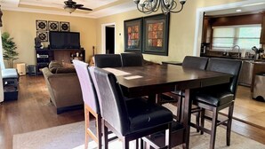 A dining area with a large wooden table and black chairs, a ceiling fan, and a chandelier.