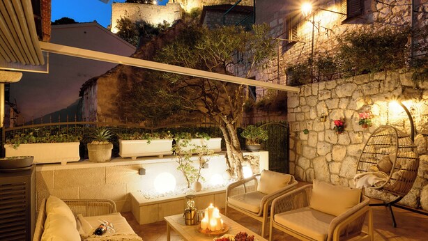 Eine Terrasse im Freien mit Korbmöbeln, einer Steinmauer und Blick auf einen historischen Turm.