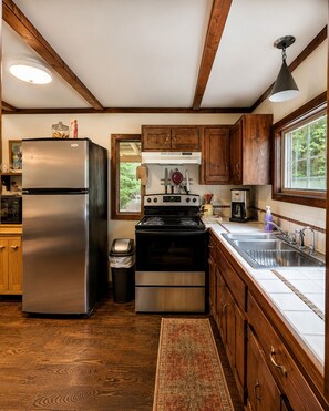 Una cocina con armarios de madera, un refrigerador de acero inoxidable, una estufa y un ventanal con vistas a la vegetación.