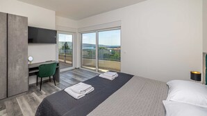 Ein modernes Hotelzimmer mit Bett, Schreibtisch, Sessel, Fernseher und einem Balkon mit Blick.