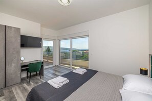 A modern hotel room with a bed, a desk, a chair, a TV, and a balcony with a view. - Holiday house VILLA PATRICK with pool, jacuzzi and sauna (Kornić)