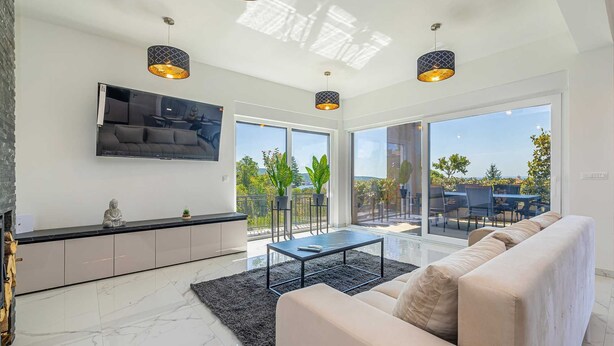 Ein modernes Wohnzimmer mit Sofa, Fernseher und Essbereich, ausgestattet mit großen Fenstern und einem Balkon.