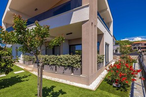 A modern building with a flat roof, large windows, and a well-maintained garden with various plants and flowers. - Holiday house VILLA PATRICK with pool, jacuzzi and sauna (Kornić)