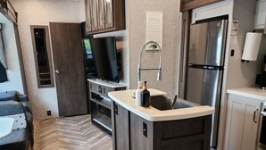 Una cocina compacta con piso de espiga, una isla integrada, un refrigerador y un televisor.