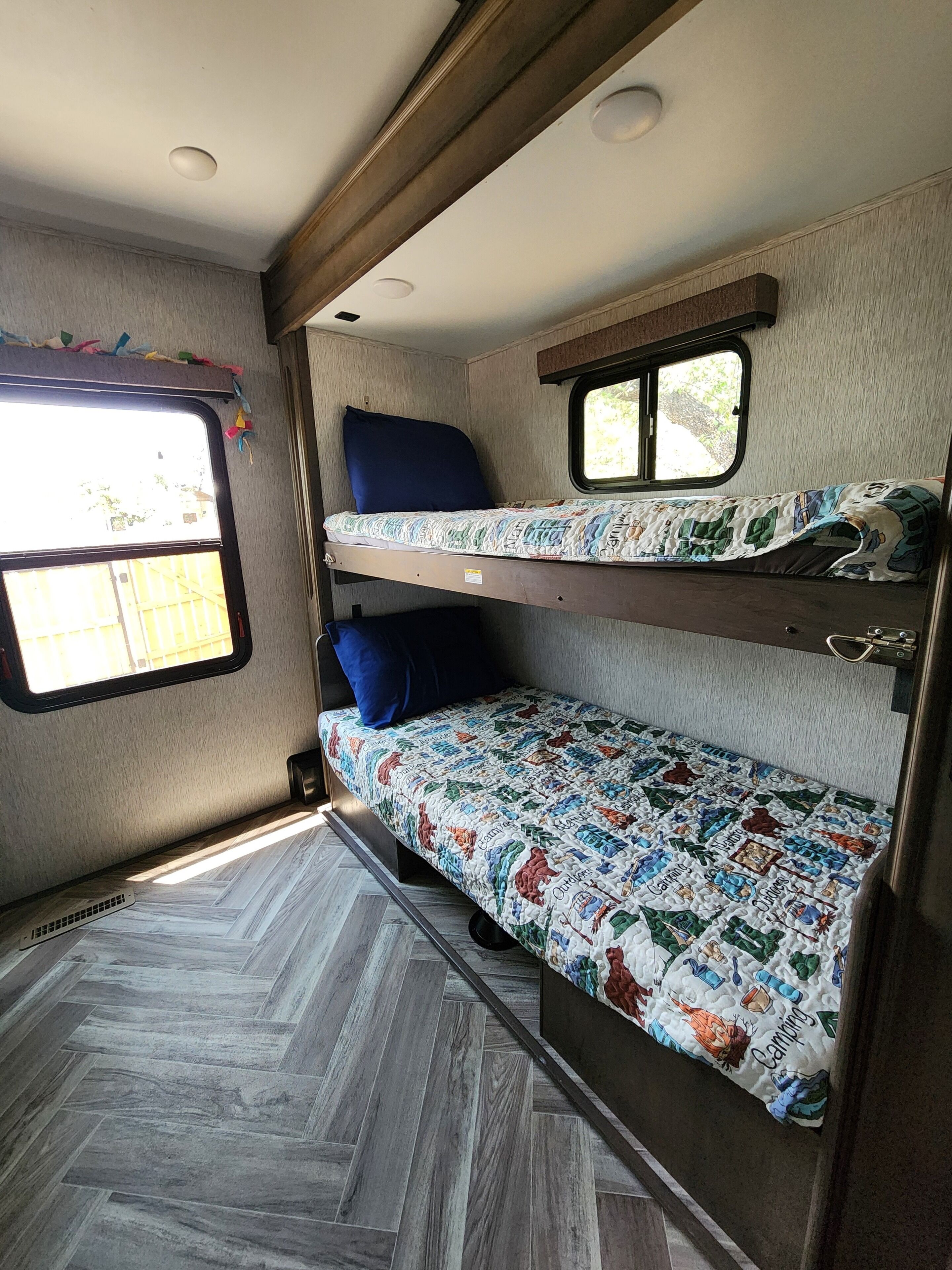 Ein Stockbett mit Fenster, einem kleinen Tisch und einem Fußboden mit Fischgrätenmuster.