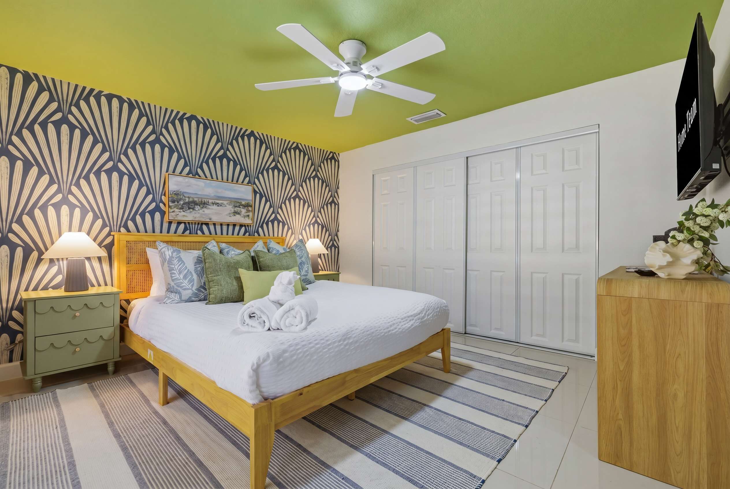 Une chambre à coucher comprenant un lit, des tables de chevet, un ventilateur de plafond, un téléviseur et une armoire.