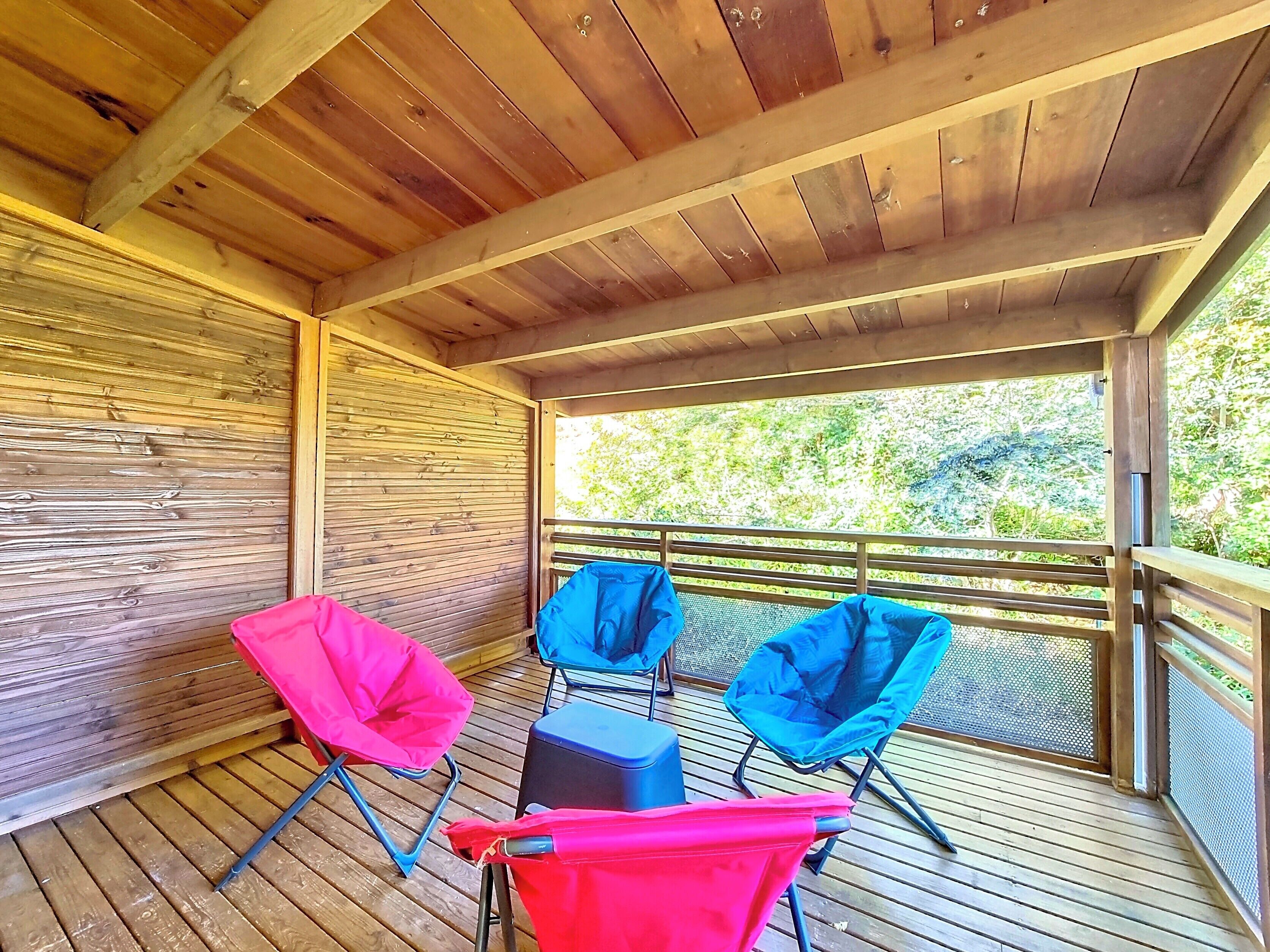 Un espace extérieur abrité doté d’un plancher en bois, de rampes en métal et de deux chaises pliantes.