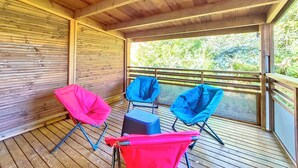 Un espacio al aire libre techado con piso de madera, barandas de metal y dos sillas plegables.
