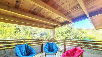 A covered outdoor deck with a wooden ceiling and metal railing. There are three chairs, two blue and one pink, on the deck.