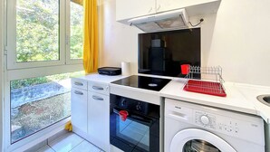 Una cocina compacta con horno integrado, lavadora y ventana con cortinas.