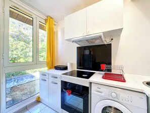 Eine kompakte Küche mit Einbauofen, Waschmaschine und einem fenster mit Vorhängen.