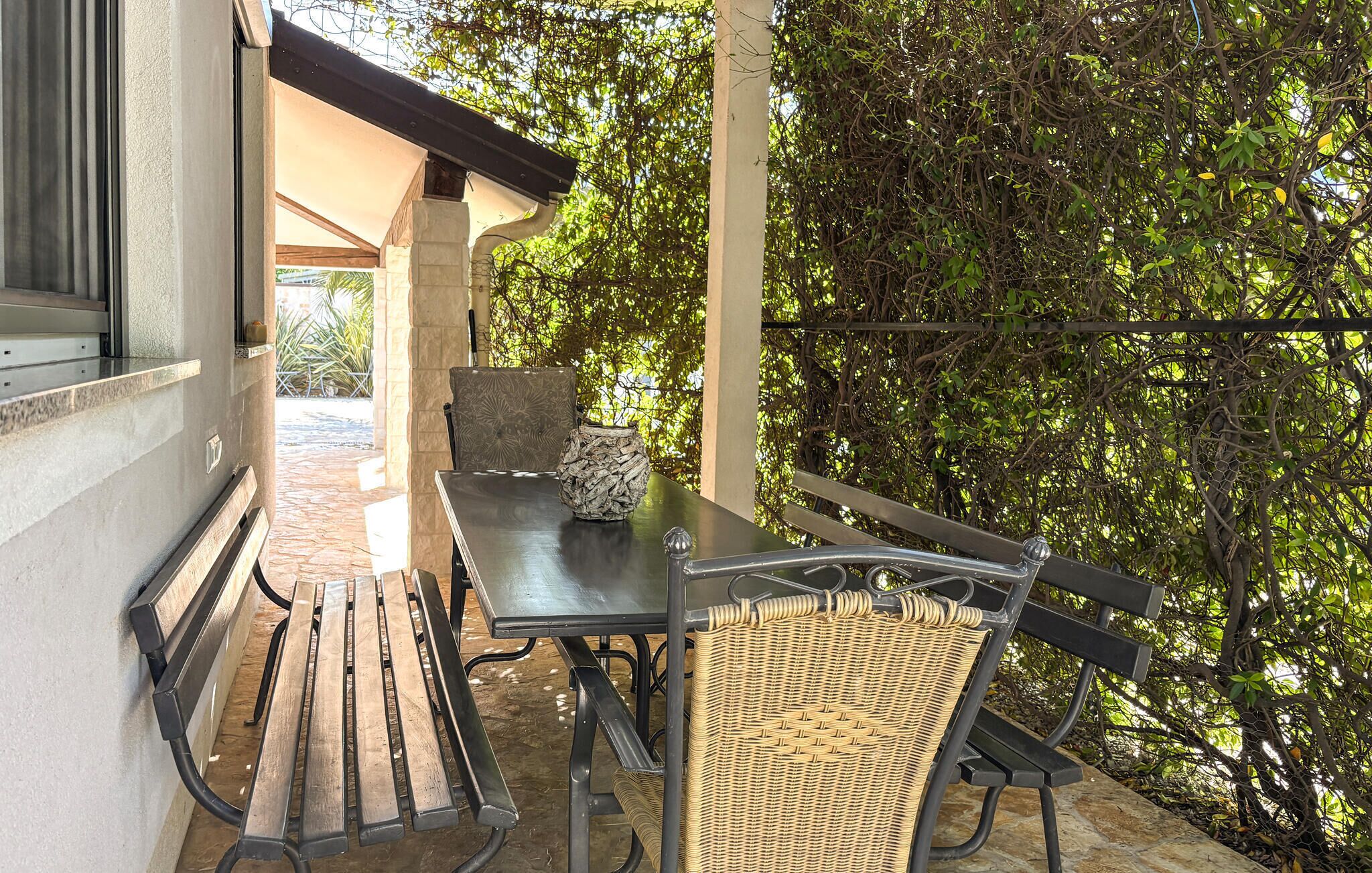 An outdoor patio with a table and chairs, surrounded by a stone wall and lush greenery.