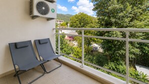 Un balcón con dos sillones de descanso, equipos de aire acondicionado y vistas a zonas verdes y edificios.