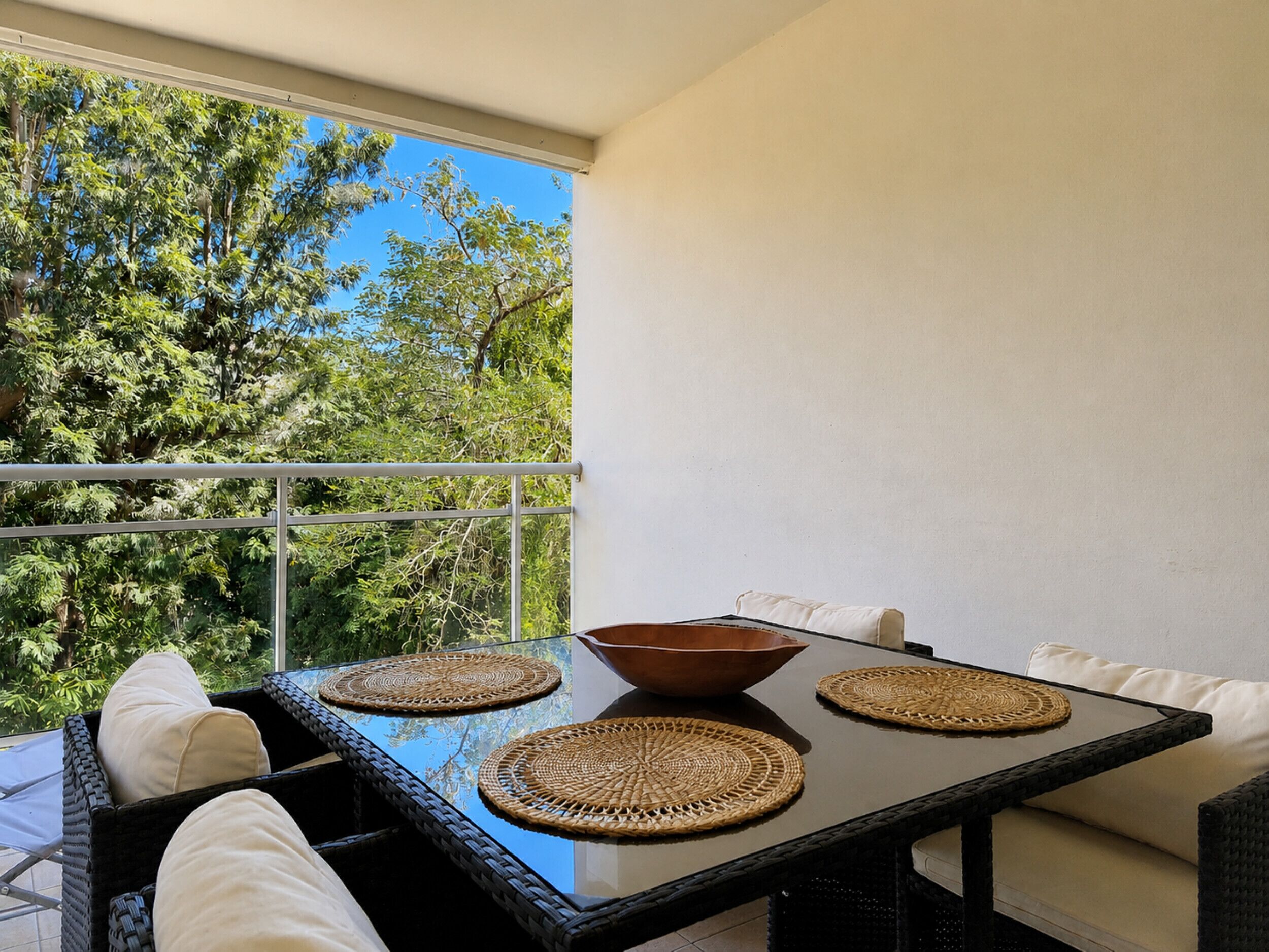 A balcony with a glass table, woven placemats, and wicker furniture.