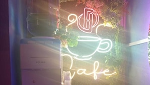 A neon sign with a coffee cup design, a water dispenser, and a white box labeled 'VÖLKER' on a wooden table.